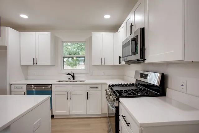 a kitchen with stainless steel appliances granite countertop a sink stove a refrigerator and white cabinets