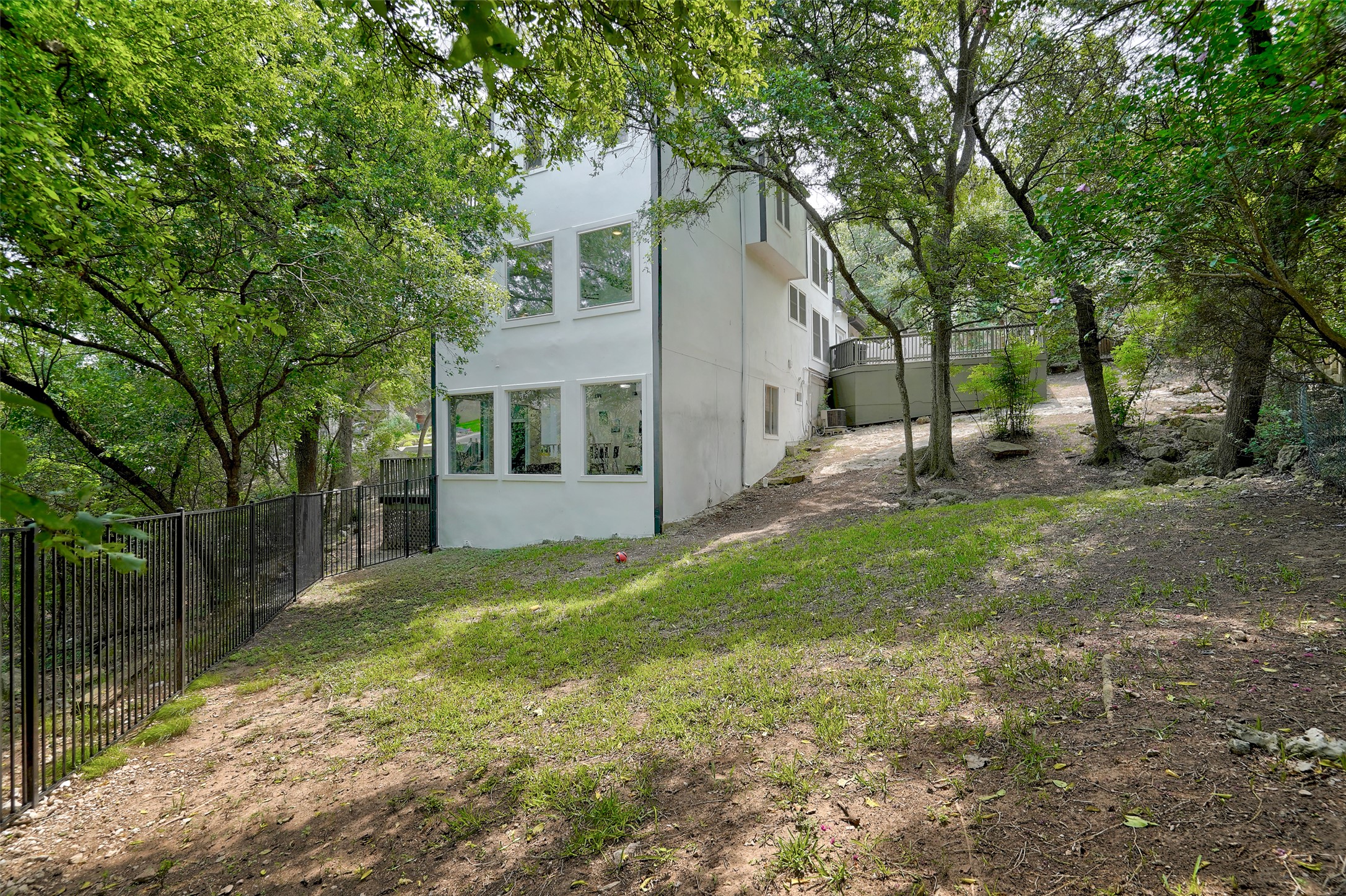 8804 Mountain Ridge Drive, Unit B Austin, TX 78759 - Photo 16 of 17 A private, tree-lined yard with a black metal fence, leading to a charming white residence with ample windows.