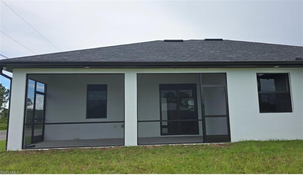 3300 3rd Street Southwest Lehigh Acres, FL 33976 - Photo 3 of 21 Back of property featuring a shingled roof, a lawn, a sunroom, and stucco siding