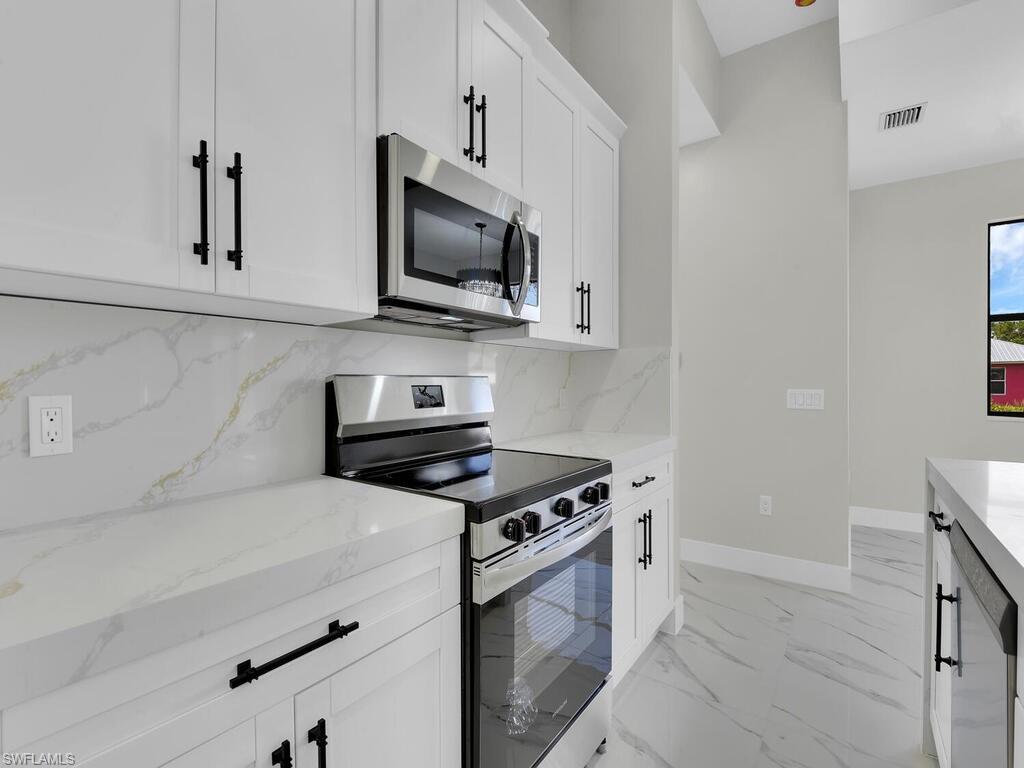 3300 3rd Street Southwest Lehigh Acres, FL 33976 - Photo 7 of 21 Kitchen with stainless steel appliances, tasteful backsplash, white cabinetry, and light stone counters