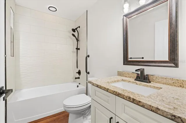 a bathroom with a granite countertop sink toilet mirror and a bathtub