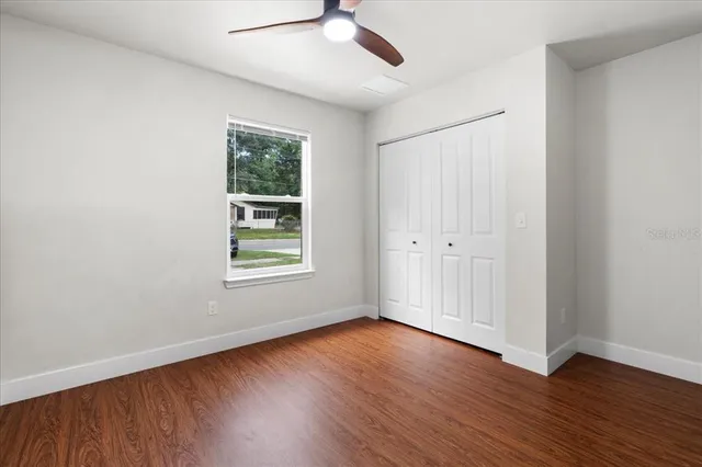 an empty room with wooden floor chandelier fan and windows