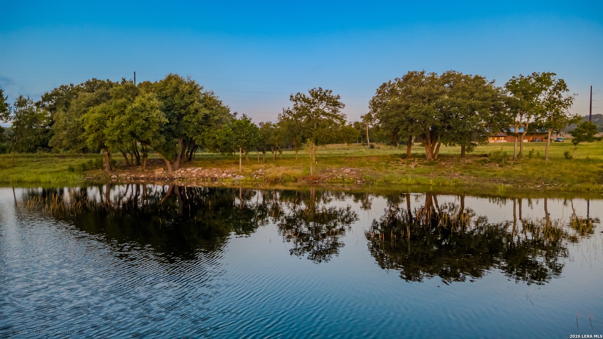 3259 Schumann Road Stonewall, TX 78671 - Photo 3 of 36 A tranquil lake view bordered by lush trees and verdant landscape.