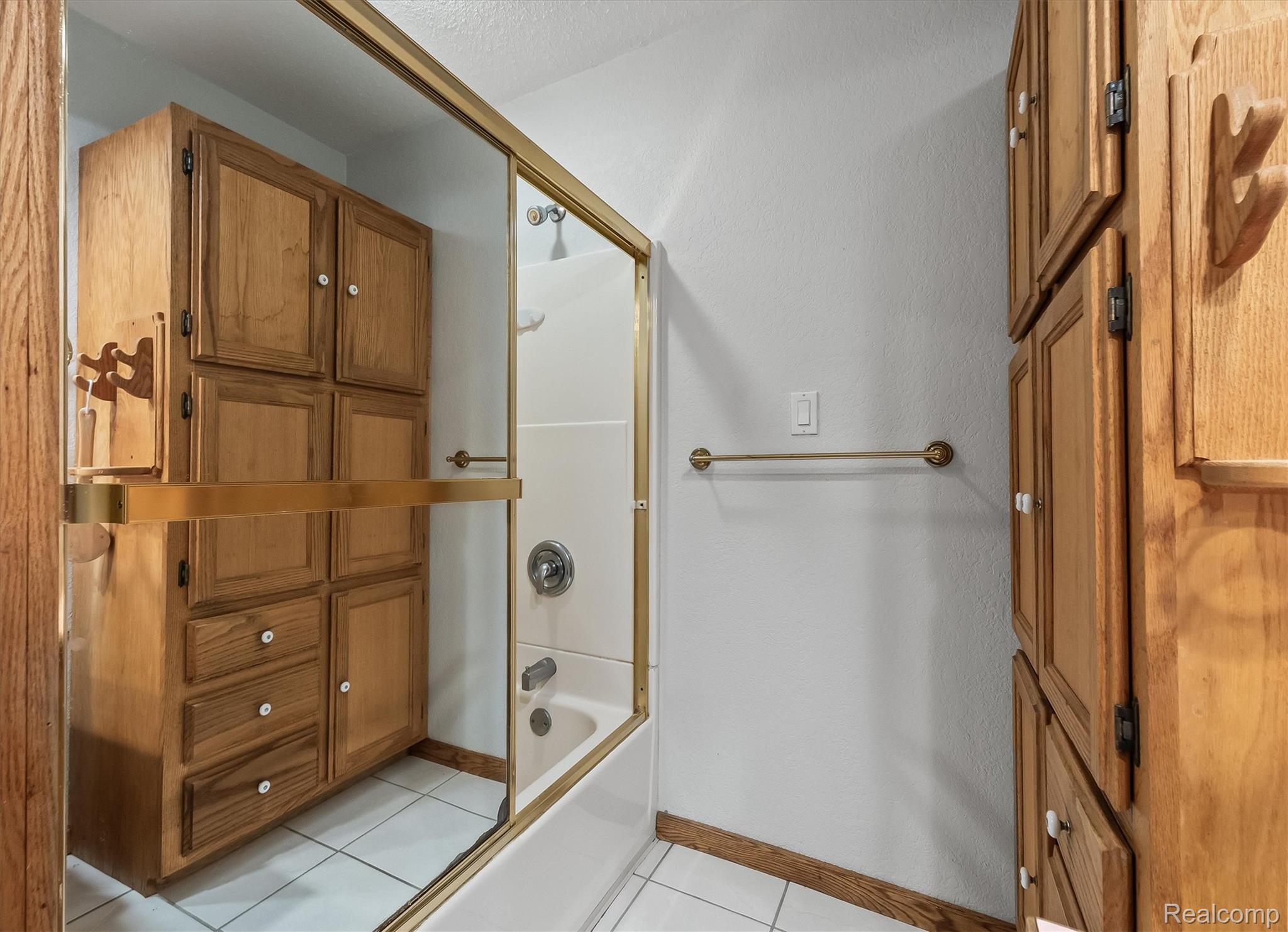 3553 North State Road Owosso, MI 48867 - Photo 24 of 45 Built-in cabinetry with wood-finish doors and drawers, white tiled flooring, and a bathtub with a sliding glass enclosure
