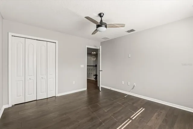 an empty room with wooden floor ceiling fan and windows