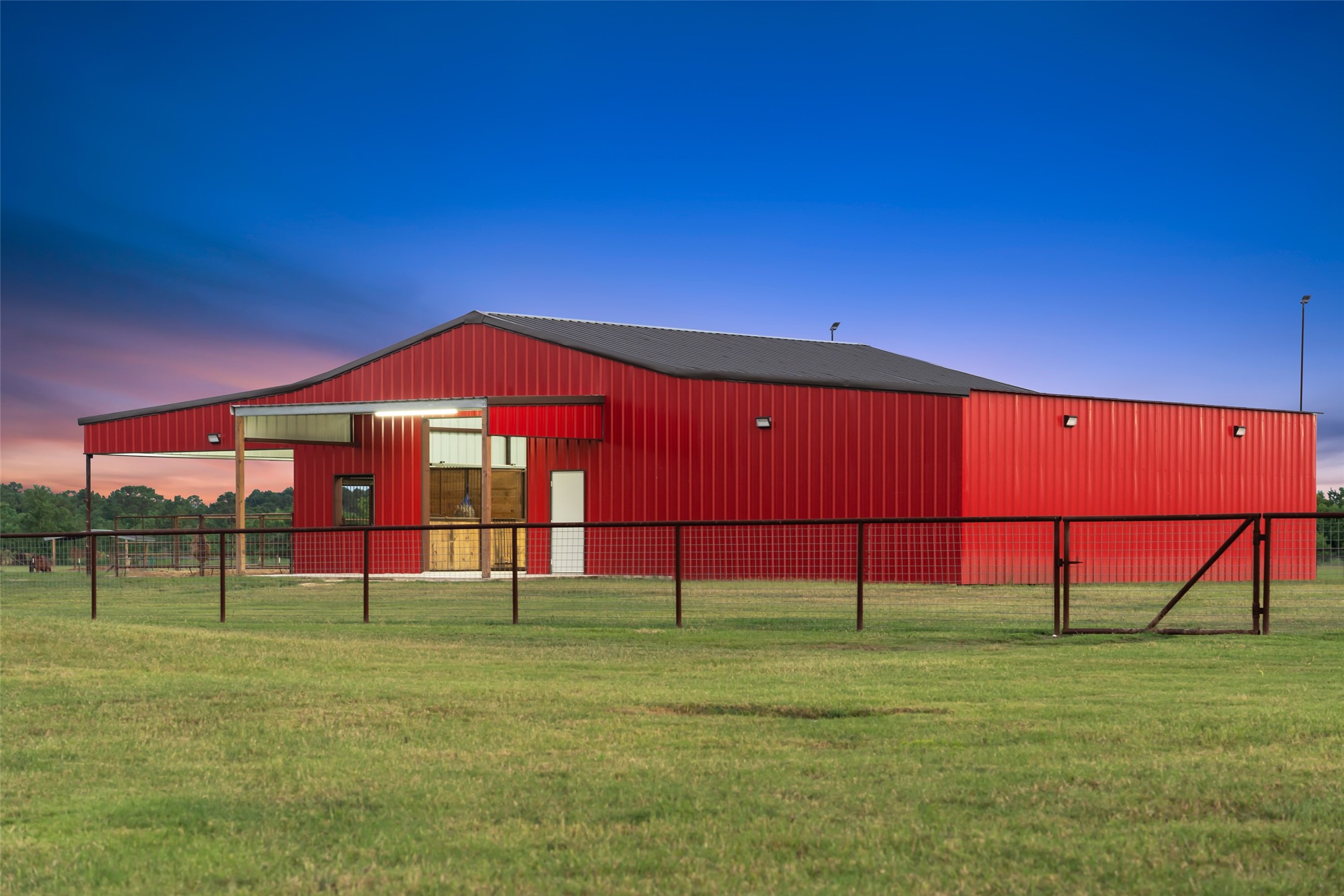 1402 Eagle Ferry Road Anahuac, TX 77514 - Photo 10 of 48 Evening lighting showcases the barn’s striking red exterior, secure fencing, and accessible layout. This functional design with multiple entry points, welded fencing, and covered areas for livestock provides comfort and easy handling.