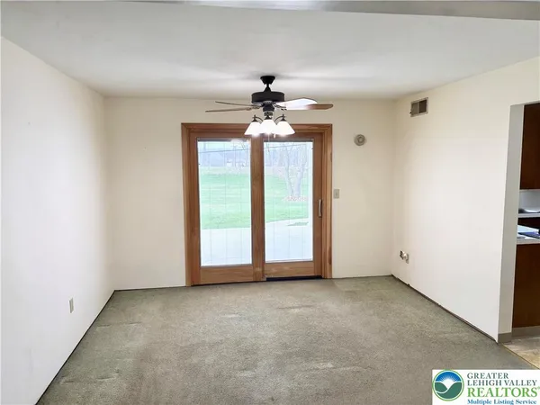 an empty room with chandelier fan and windows