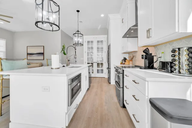 a kitchen with stainless steel appliances kitchen island granite countertop a stove a sink a refrigerator and white cabinets with wooden floor