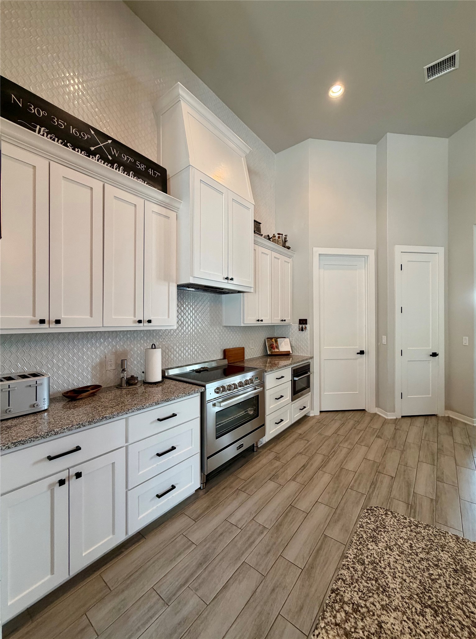 14302 Summit View Drive, Unit 4 Leander, TX 78641 - Photo 8 of 40 Kitchen featuring white cabinets, stainless steel stove, wood tiled floors, light stone counters, and decorative backsplash
