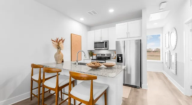 a kitchen with stainless steel appliances granite countertop a refrigerator a stove a microwave oven a sink with island chairs and wooden floor