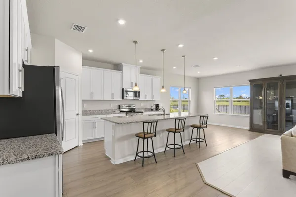 a kitchen with stainless steel appliances granite countertop a stove a refrigerator a sink a dining table and chairs with wooden floor