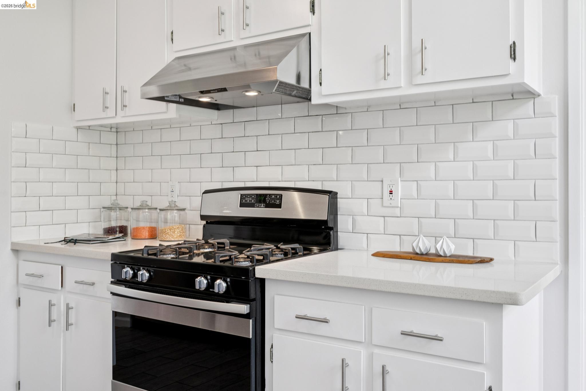 1340 Henry Street Berkeley, CA 94709 - Photo 19 of 52 White kitchen featuring subway tile backsplash, white cabinetry, a stainless steel range hood, stone-finish countertops, and a stainless steel gas range