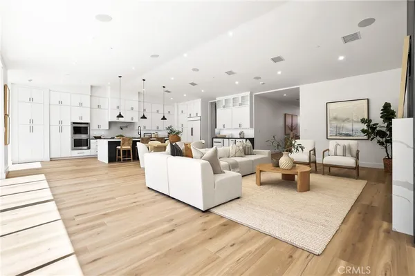 a large living room with stainless steel appliances kitchen island granite countertop a large kitchen island a stove a sink a refrigerator white cabinets and wooden floor