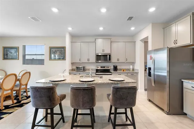 a kitchen with stainless steel appliances granite countertop a sink a stove a refrigerator cabinets and chairs