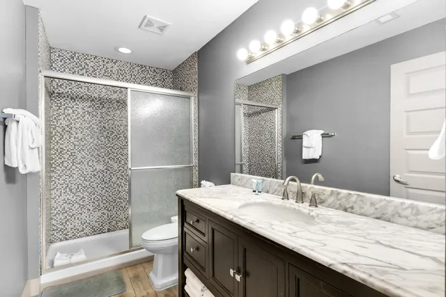 a bathroom with a granite countertop sink a toilet a mirror a vanity and shower