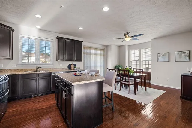 a kitchen with stainless steel appliances granite countertop a stove top oven a sink dishwasher a dining table and chairs with wooden floor