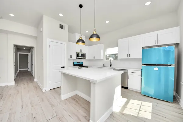 a kitchen with stainless steel appliances granite countertop a refrigerator a sink dishwasher a stove and white cabinets with wooden floor