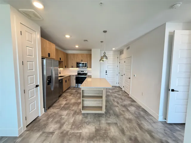 a large white kitchen with stainless steel appliances granite countertop a refrigerator oven a stove top oven with white cabinets and wooden floor