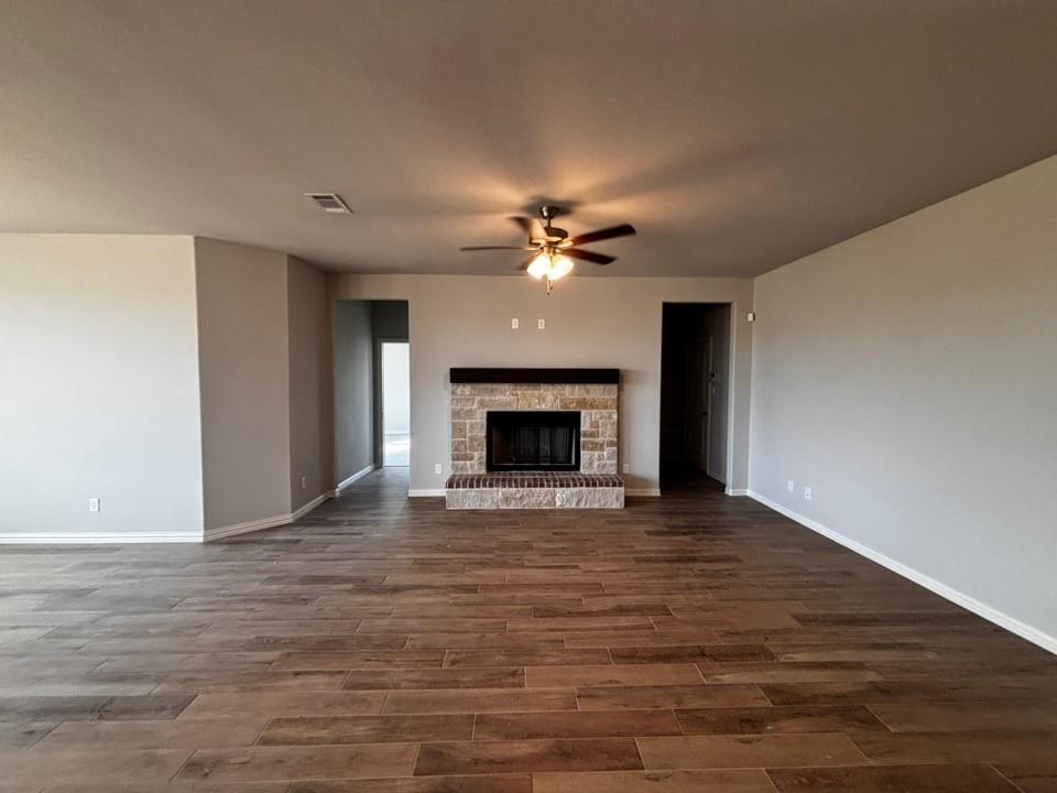 128 Pheasant Run Drive Rhome, TX 76078 - Photo 7 of 14 Spacious living area featuring wood-finish flooring, a stone fireplace with a dark wood mantel, and a ceiling fan with integrated lighting