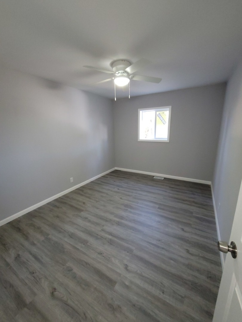 133 Kingston Road Bolingbrook, IL 60440 - Photo 9 of 19 an empty room with wooden floor chandelier fan and windows