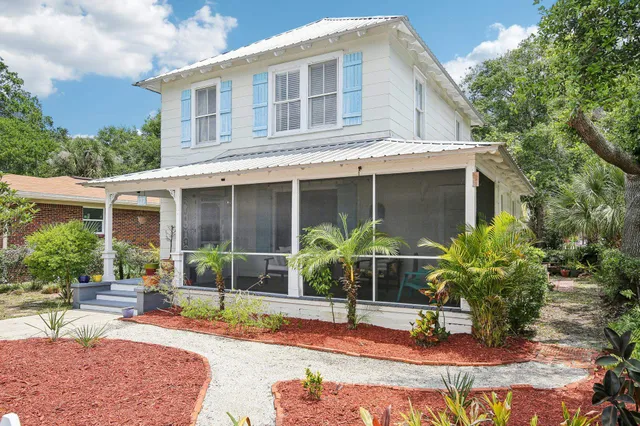 a view of a white house next to a yard with plants and trees