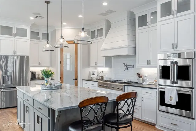 a kitchen with stainless steel appliances kitchen island granite countertop a sink a stove a refrigerator cabinets and chairs