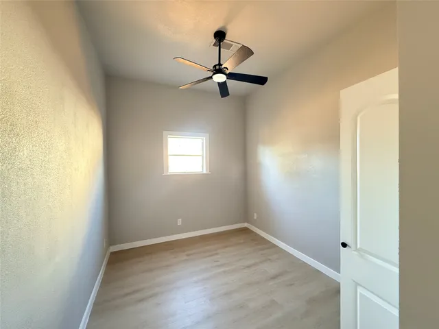 an empty room with wooden floor ceiling fan and windows