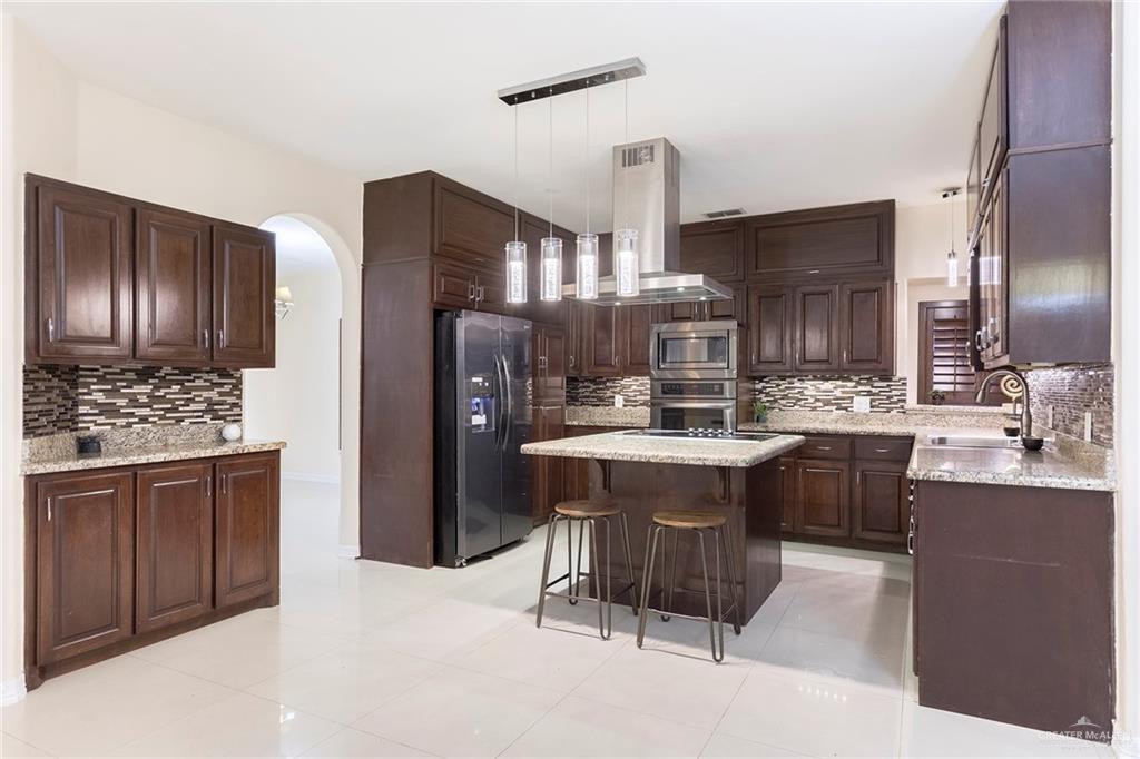 2001 Quail Lane Mission, TX 78572 - Photo 5 of 28 Expansive kitchen featuring dark wood cabinetry, light-toned countertops, tile flooring, stainless steel appliances, and a central island with pendant lighting