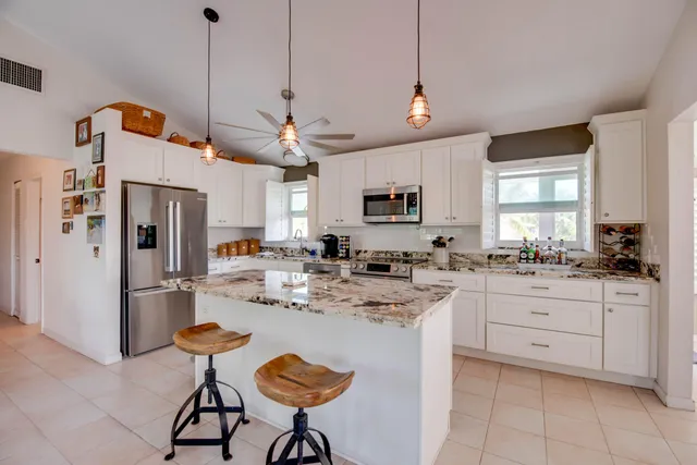 a kitchen with stainless steel appliances kitchen island granite countertop a sink a stove a refrigerator cabinets and chairs
