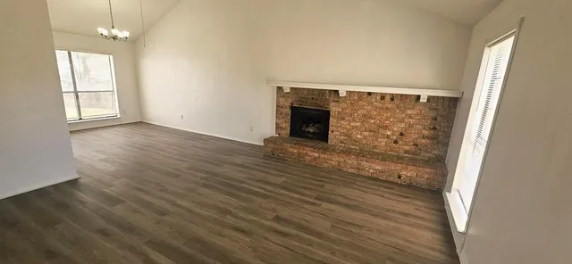 an empty room with wooden floor fireplace and windows
