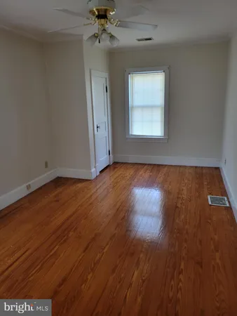 an empty room with wooden floor chandelier fan and windows