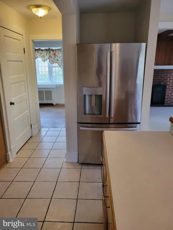 a view of a refrigerator in kitchen and an empty room with wooden floor