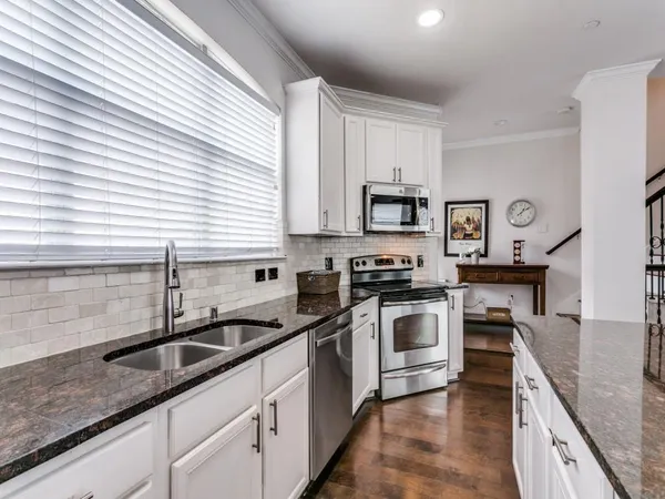 a kitchen with stainless steel appliances granite countertop white cabinets a sink and a stove