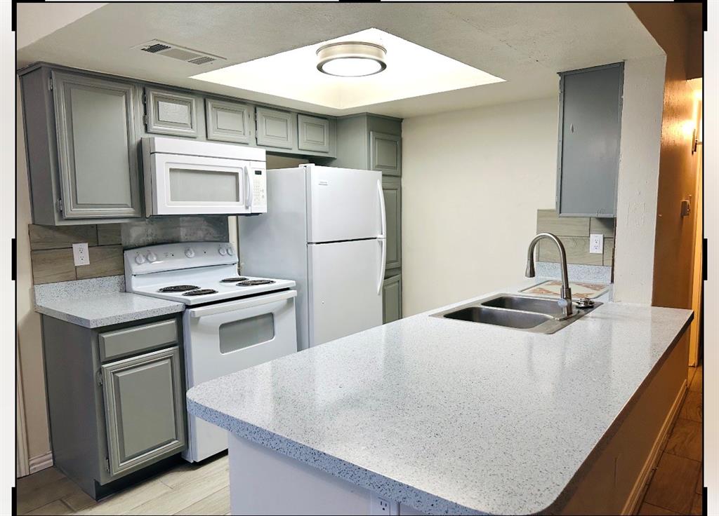 4472 Chaha Road, Unit 104 Garland, TX 75043 - Photo 5 of 5 Kitchen featuring light gray cabinetry, speckled white countertops, a double basin stainless steel sink with a gooseneck faucet, a light wood-finish backsplash, and an overhead microwave