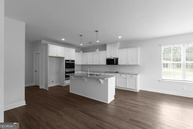 a kitchen with stainless steel appliances kitchen island granite countertop a stove a sink a refrigerator and white cabinets with wooden floor