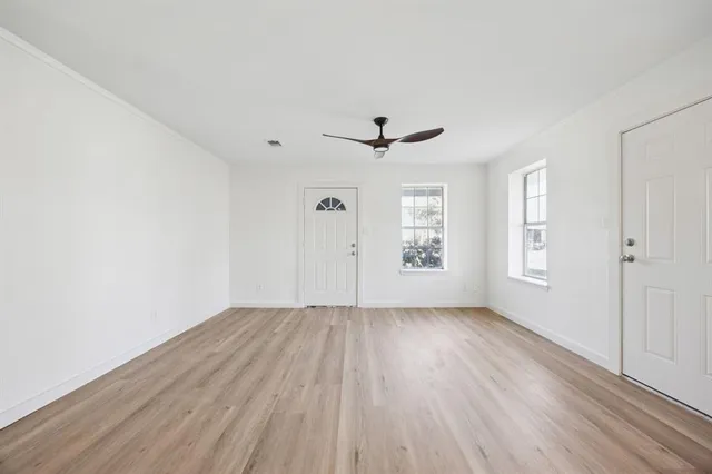 an empty room with wooden floor chandelier fan and windows