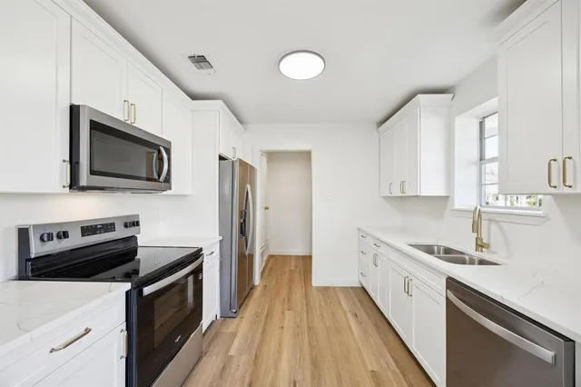 a kitchen with stainless steel appliances a sink dishwasher a stove top oven a refrigerator with wooden floor and cabinets