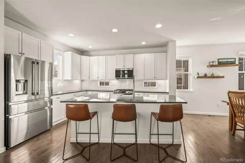 a kitchen with stainless steel appliances granite countertop a refrigerator a stove a kitchen island and chairs with wooden floor