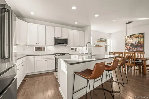 a kitchen with stainless steel appliances granite countertop a stove top oven a sink dishwasher and white cabinets with wooden floor