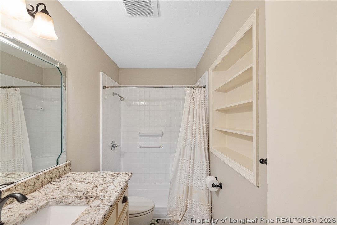 2527 Huntington Road Fayetteville, NC 28303 - Photo 31 of 39 a bathroom with a granite countertop sink a toilet a mirror and shower