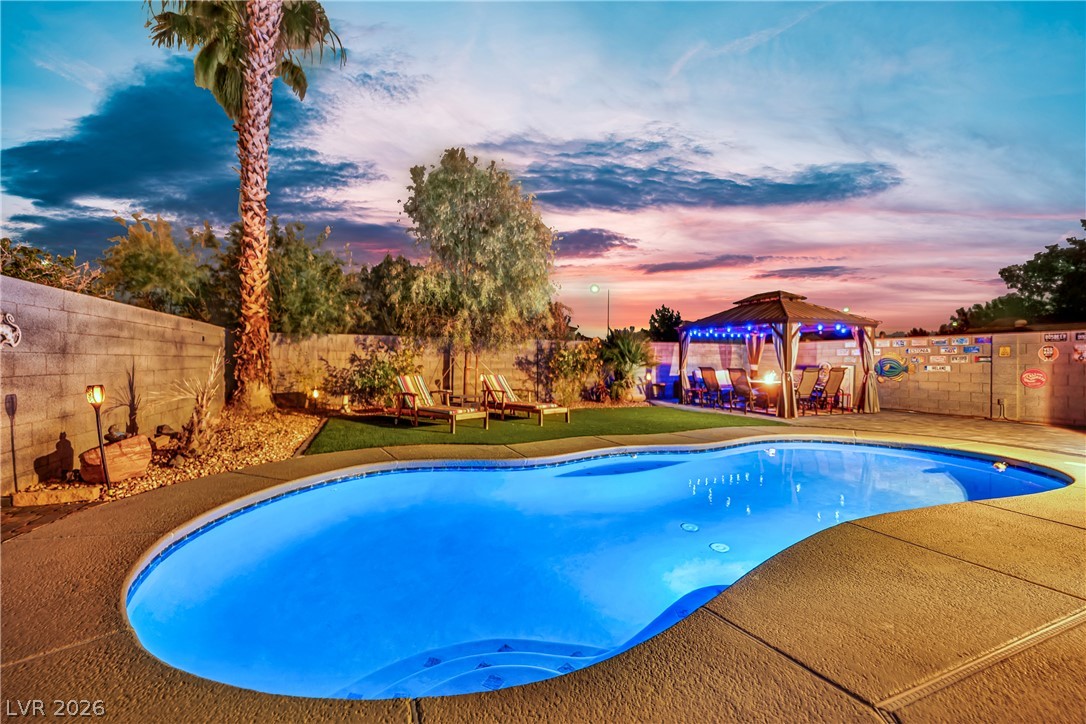 1724 Millstream Way Henderson, NV 89074 - Photo 57 of 60 An inviting backyard oasis features a freeform pool, lush landscaping, and a festive gazebo, perfect for evening gatherings.