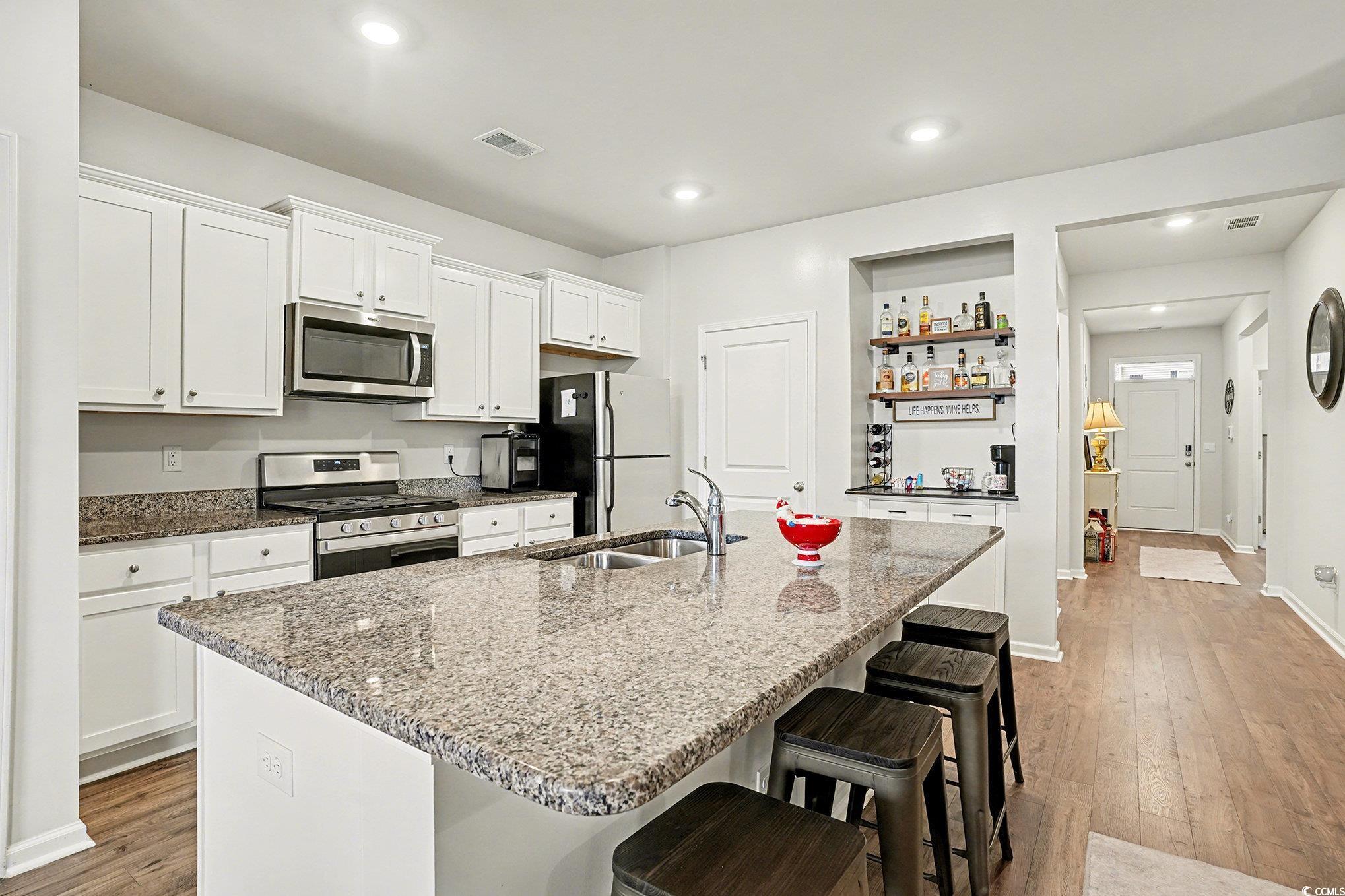 3923 Nandina Court Conway, SC 29526 - Photo 11 of 28 Kitchen featuring white cabinets, a kitchen breakfast bar, stainless steel appliances, light wood-type flooring, and dark stone counters