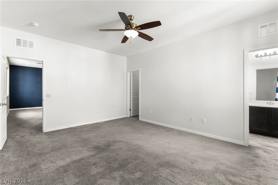 11048 Prairie Grove Road Las Vegas, NV 89179 - Photo 46 of 75 A spacious bedroom featuring soft gray carpeting and an elegant ceiling fan.