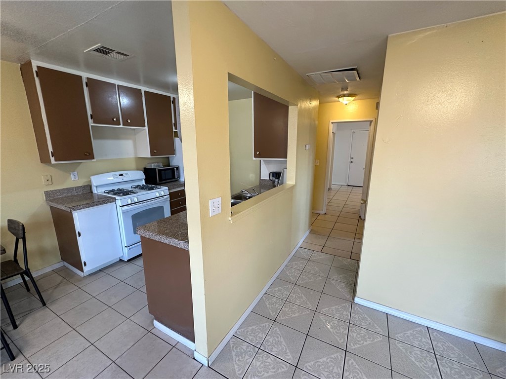 3936 Rive Gauche Street Las Vegas, NV 89115 - Photo 13 of 30 Kitchen featuring gas range gas stove, stainless steel microwave, light tile patterned floors, baseboards, and dark countertops