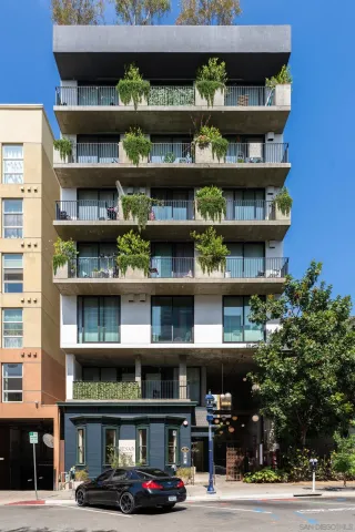 a front view of multi story building with retail shops car parked and large trees