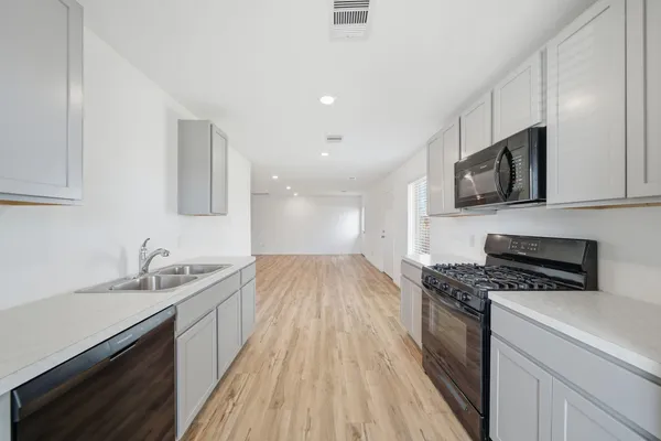 a kitchen with granite countertop a sink wooden floor stainless steel appliances and cabinets
