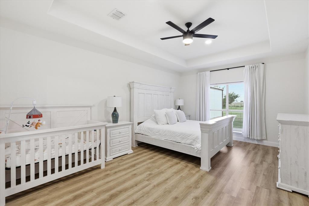 430 Ridgecrest Place Sanger, TX 76266 - Photo 13 of 40 Spacious room Primary Bedroom featuring wood-finish flooring, a tray ceiling, and a ceiling fan with integrated lighting
