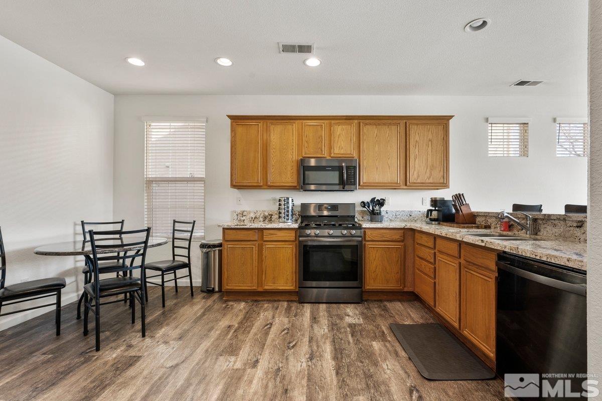 11022 Colton Drive Reno, NV 89521 - Photo 10 of 26 a kitchen with stainless steel appliances granite countertop a stove top oven a sink dishwasher a dining table and chairs with wooden floor