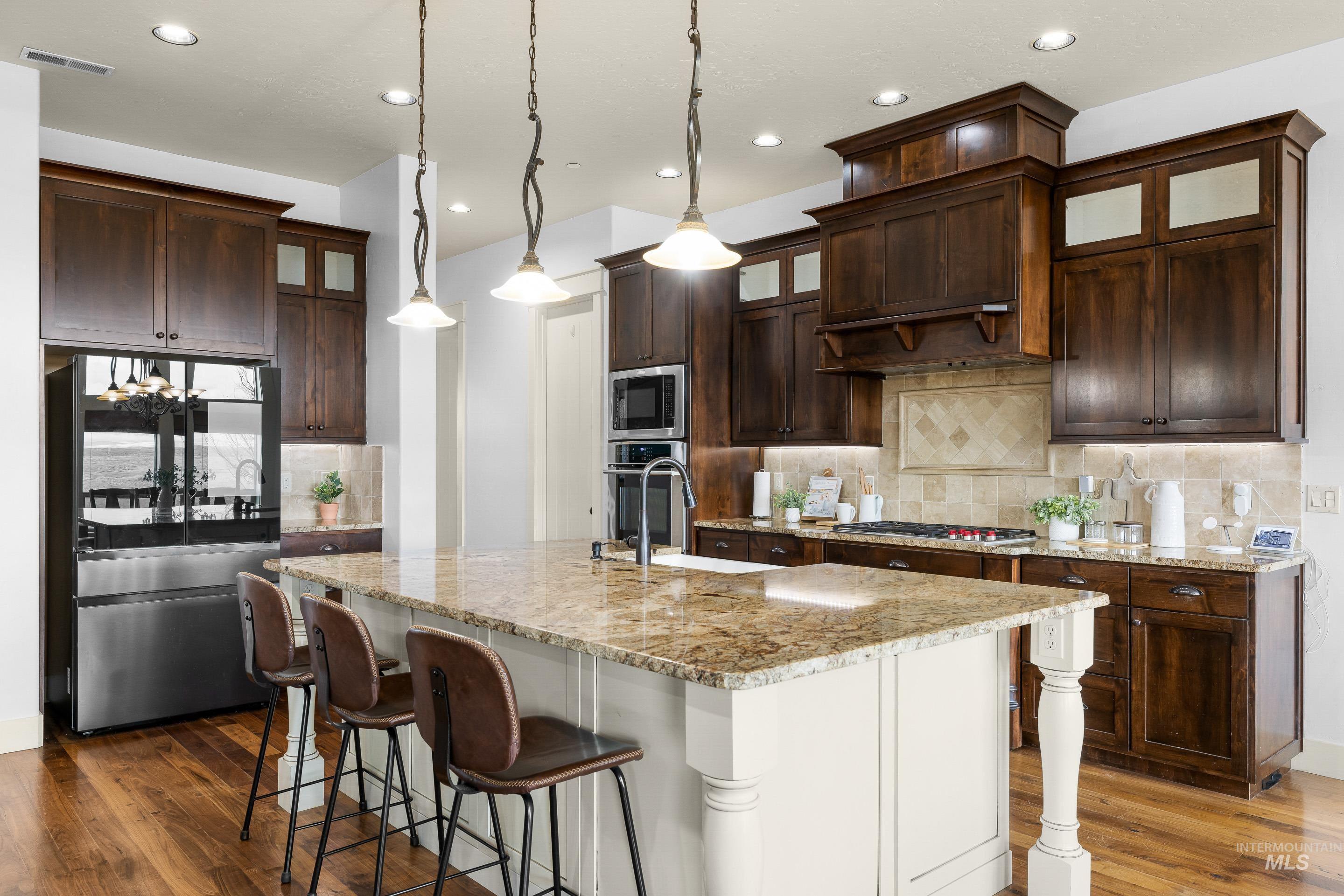 7521 North Grand Ridge Lane Eagle, ID 83616 - Photo 16 of 50 Kitchen featuring glass insert cabinets, hanging light fixtures, stainless steel appliances, a breakfast bar, and two tone cabinets