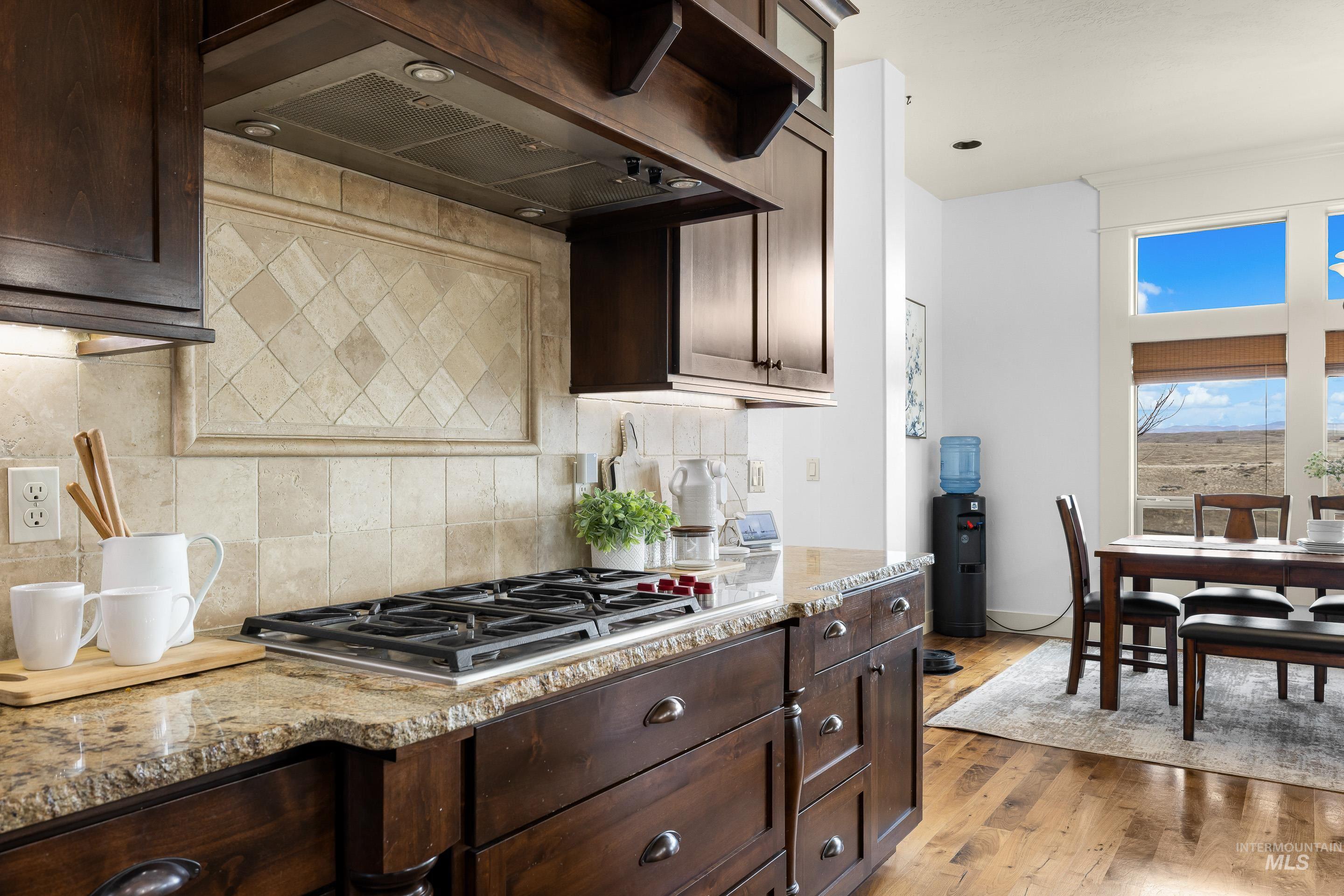 7521 North Grand Ridge Lane Eagle, ID 83616 - Photo 19 of 50 Kitchen with exhaust hood, dark wood finish cabinets, light stone counters, and tasteful backsplash